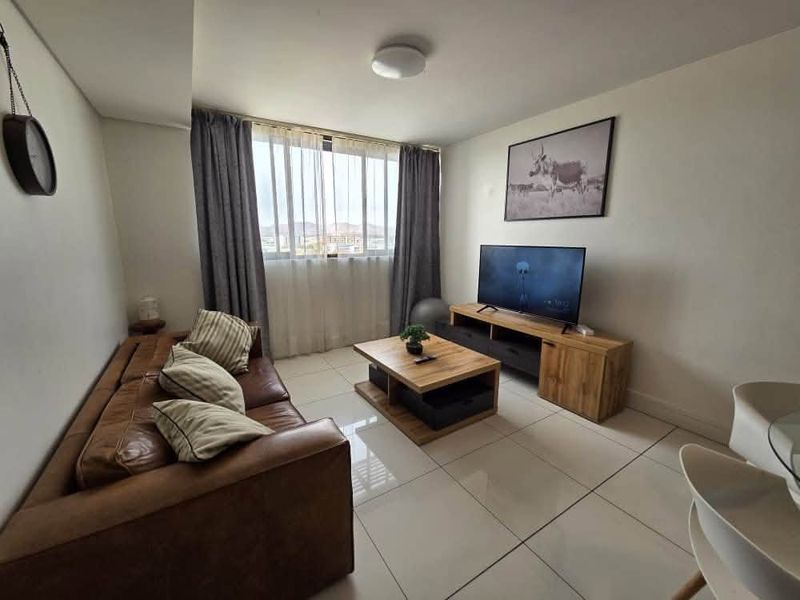 A bright and modern living room featuring large windows, neutral tiled flooring, and a clean, well-maintained interior finish.