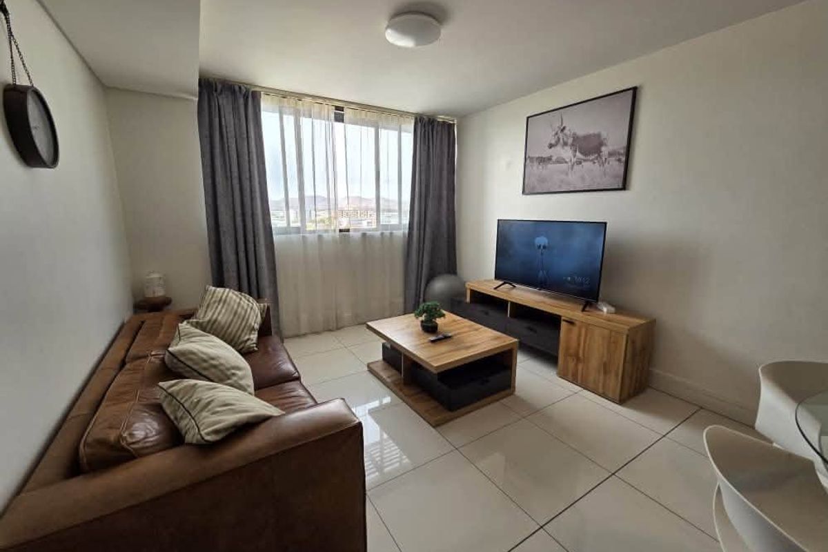 A bright and modern living room featuring large windows, neutral tiled flooring, and a clean, well-maintained interior finish.