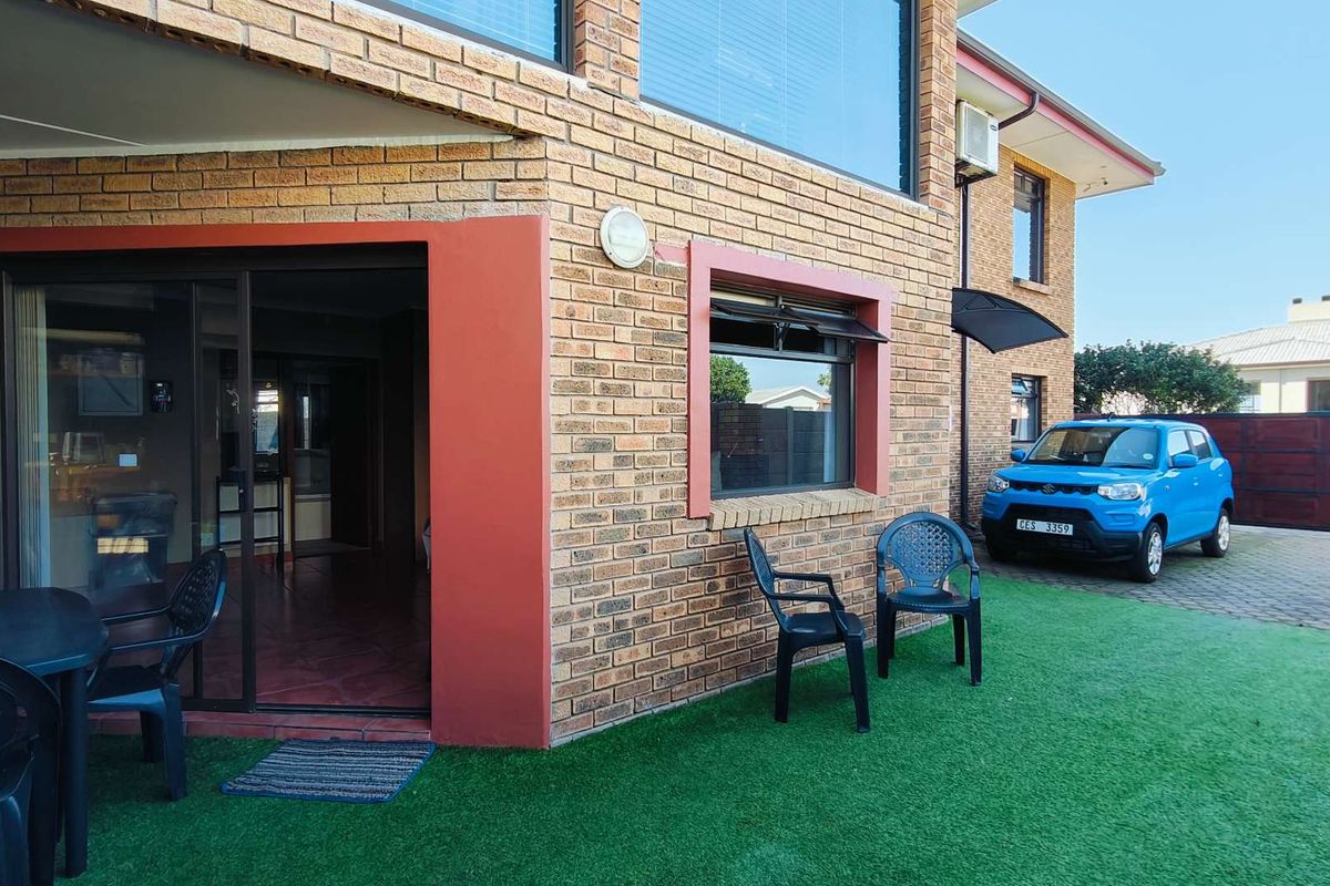 Exterior view of the house featuring a brick facade, sliding glass doors leading to an outdoor patio area, and a paved driveway.