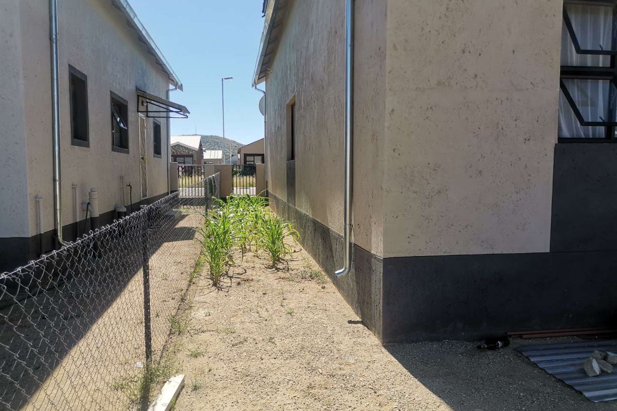 Side exterior view of the property showing the narrow passage between two buildings with metal downpipes and chain-link fencing.