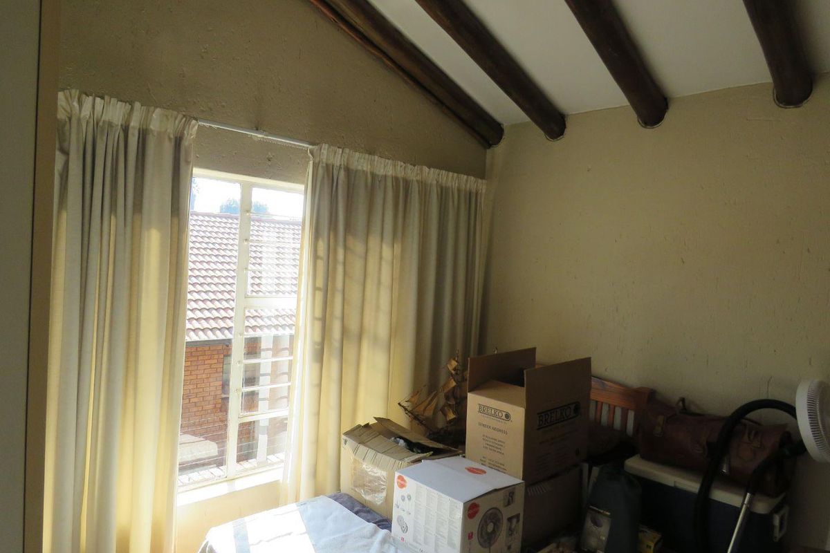 A bedroom featuring exposed timber ceiling beams and a window with natural light, offering a rustic aesthetic ready for modernization.