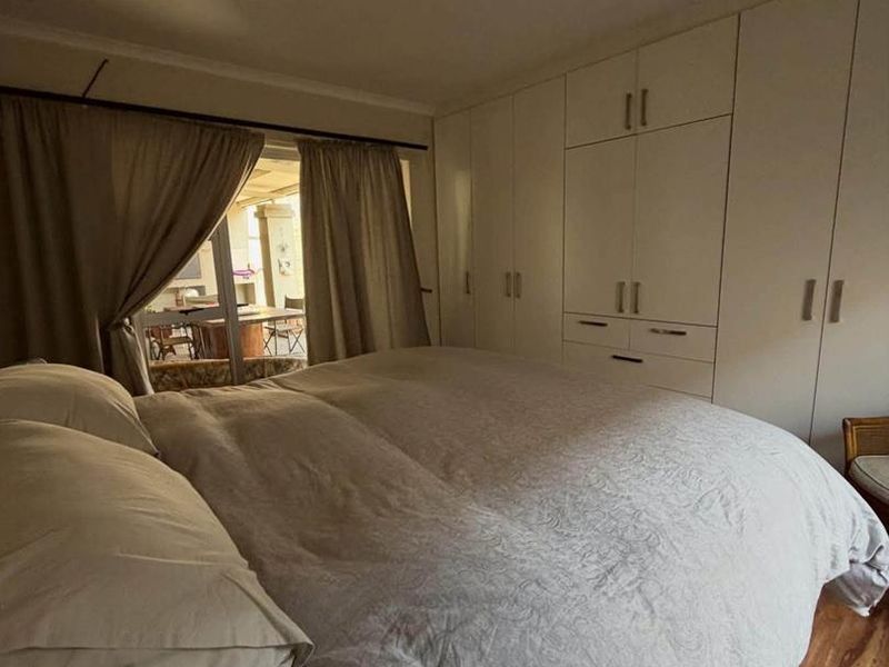 A bedroom featuring built-in cupboards, laminate flooring, and direct access to an outdoor patio area.