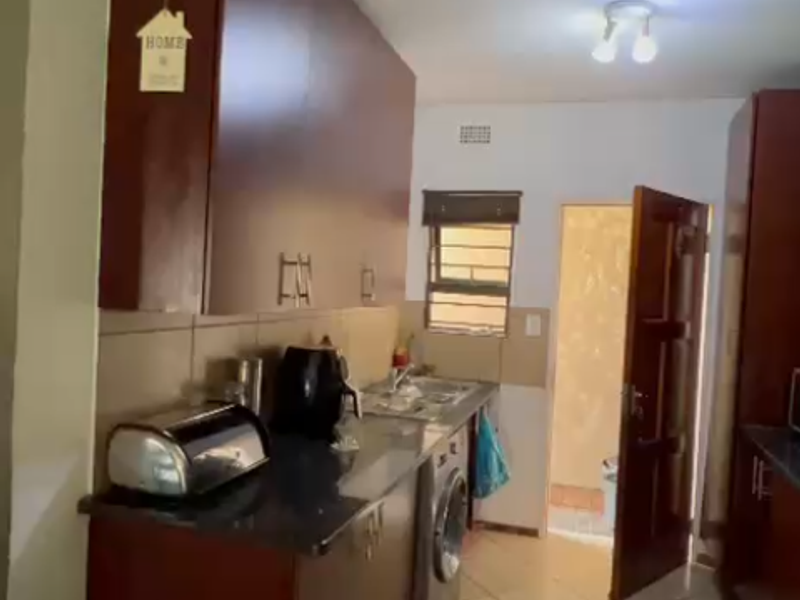 A functional kitchen featuring dark wood cabinetry, granite countertops, tiled flooring, and integrated plumbing for laundry appliances, leading to an exterior doorway.