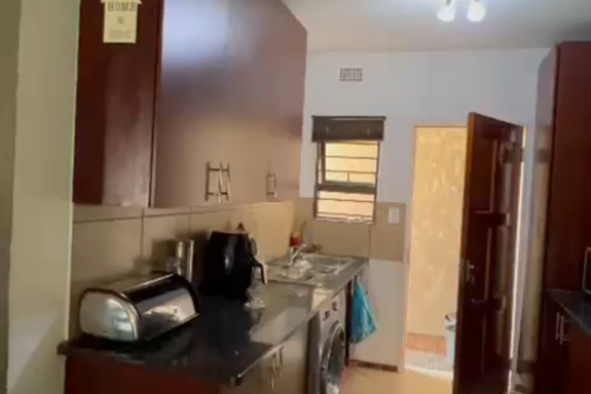 A functional kitchen featuring dark wood cabinetry, granite countertops, tiled flooring, and integrated plumbing for laundry appliances, leading to an exterior doorway.