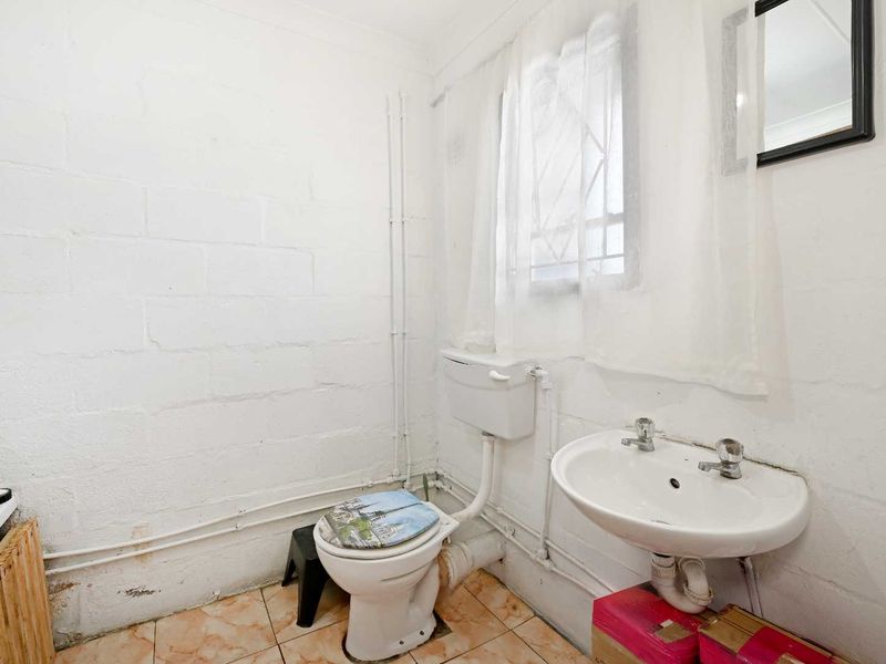A functional bathroom featuring a pedestal basin, flush toilet, and tiled flooring, with exposed plumbing and painted blockwork walls.
