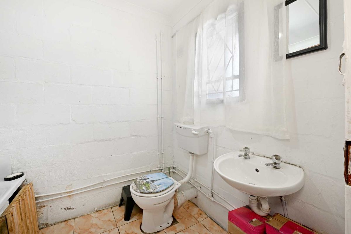 A functional bathroom featuring a pedestal basin, flush toilet, and tiled flooring, with exposed plumbing and painted blockwork walls.