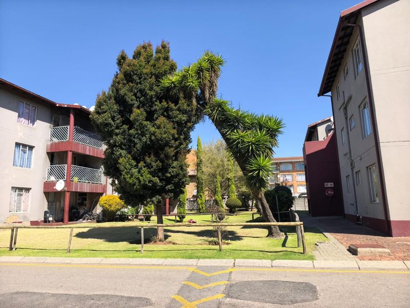 A view of the apartment complex exterior featuring a shared garden area, paved walkways, and balconies overlooking the communal grounds.