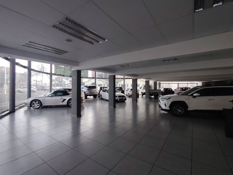 Spacious open-plan retail showroom featuring large glass windows, tiled flooring, and a suspended ceiling with recessed lighting, ideal for vehicle display.