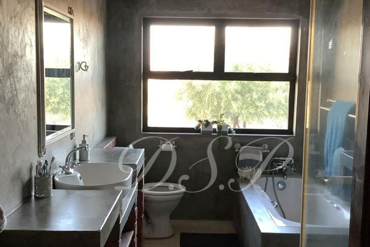 Modern industrial-style bathroom featuring a concrete vanity with vessel sink, built-in bathtub, and a glass-enclosed shower with polished concrete flooring.