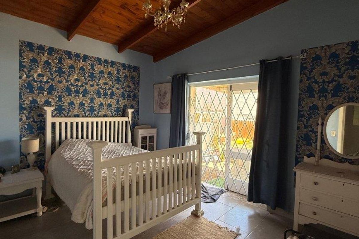 Spacious bedroom featuring a high timber-beamed ceiling, tiled flooring, and sliding glass doors with security gates leading to the exterior.