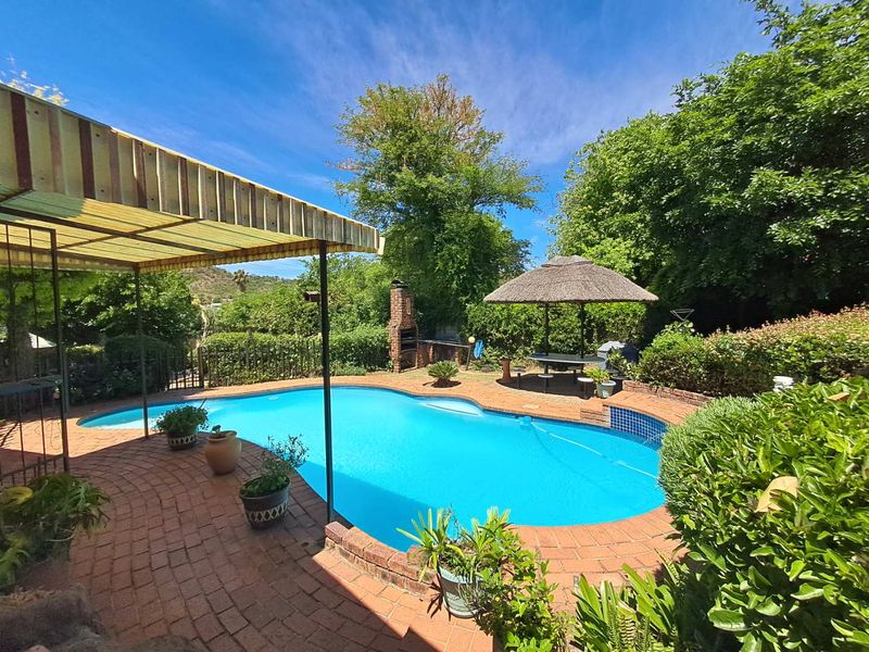 Outdoor pool area featuring a swimming pool, brick paved surround, built-in brick braai, and a covered patio space with a thatched umbrella.
