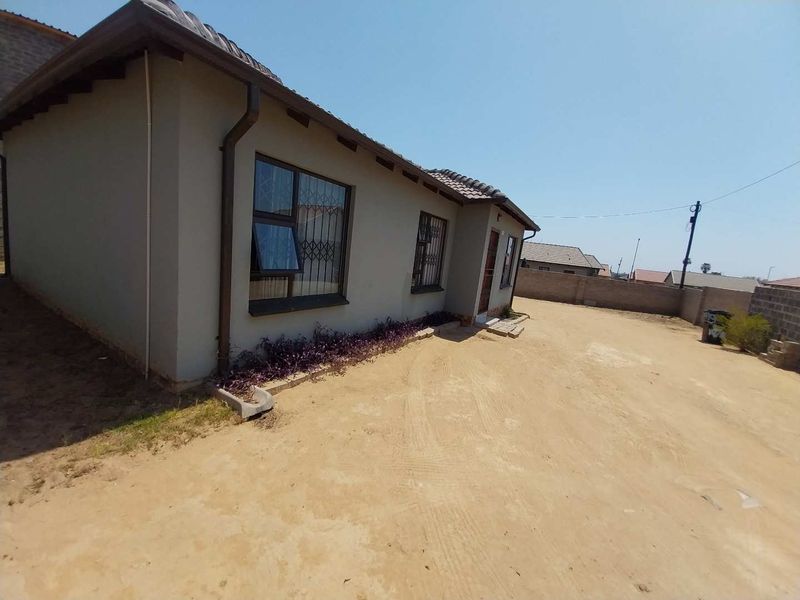 Rear view of the property featuring a tiled roof, aluminium window frames with security bars, and a large unpaved yard area.