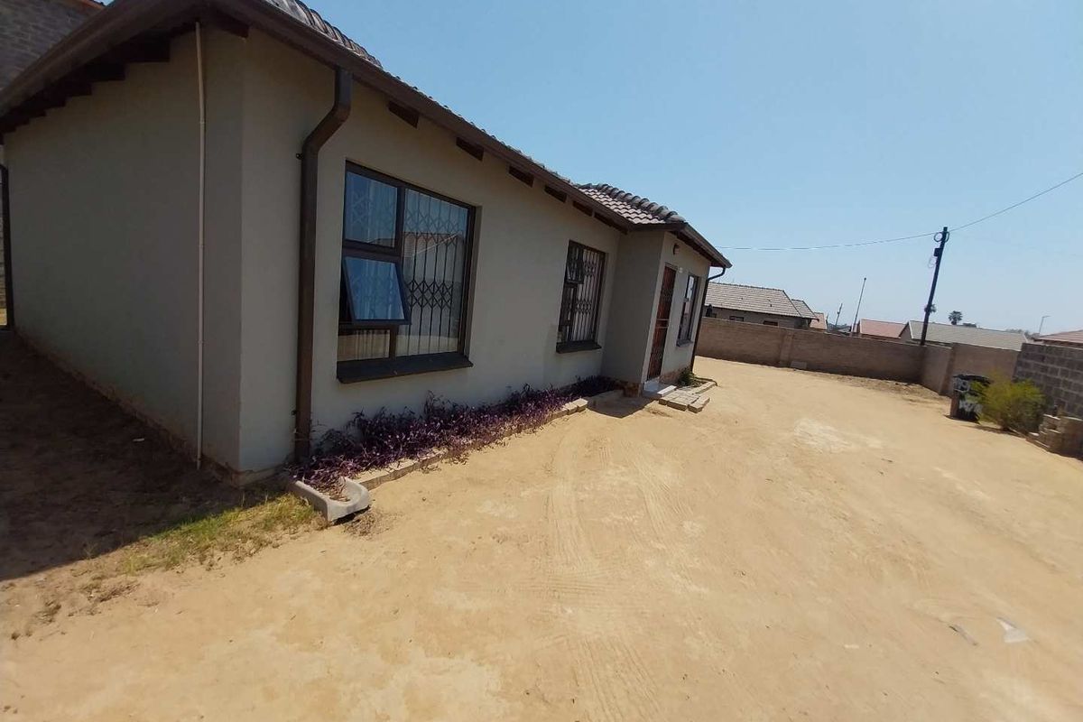 Rear view of the property featuring a tiled roof, aluminium window frames with security bars, and a large unpaved yard area.