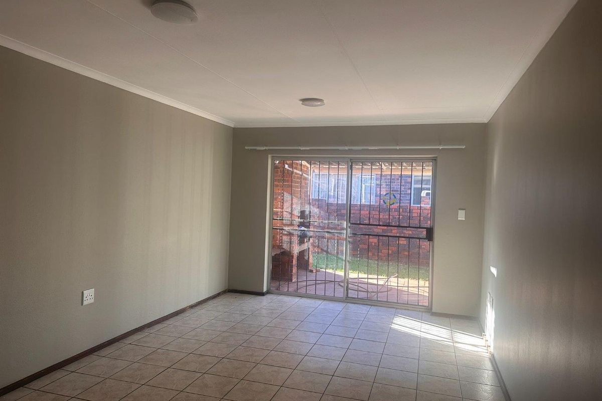 An empty living room featuring tiled flooring and sliding glass doors with security gates, providing direct access to the rear patio area.