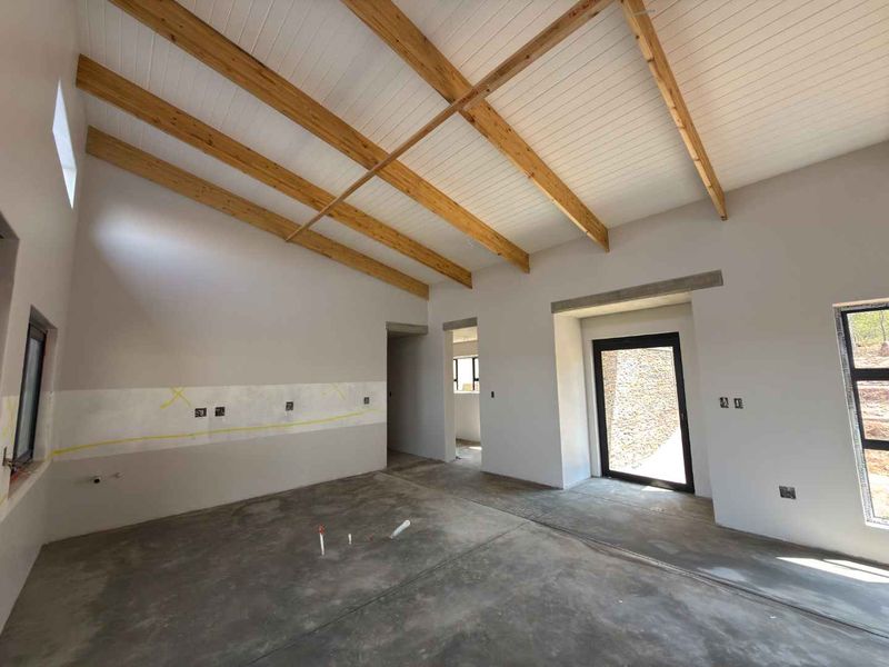 An unfinished kitchen space featuring exposed timber ceiling beams, concrete flooring, and large aluminium-framed windows and doors, ready for final cabinetry and finishes.
