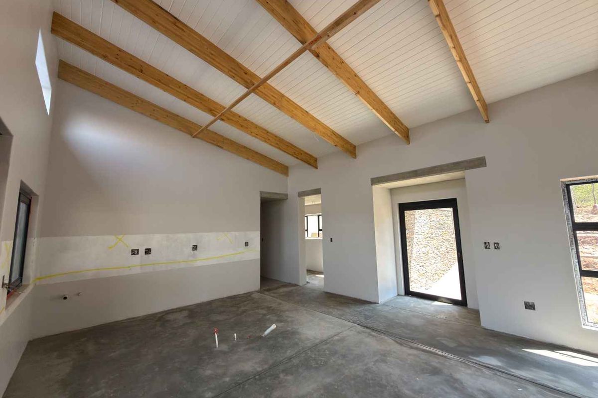 An unfinished kitchen space featuring exposed timber ceiling beams, concrete flooring, and large aluminium-framed windows and doors, ready for final cabinetry and finishes.