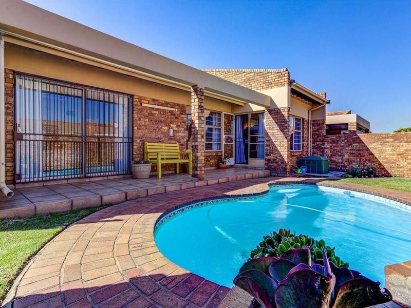 A well-maintained outdoor pool area featuring a paved deck, covered patio space, and brick boundary walls, ideal for outdoor relaxation and entertainment.