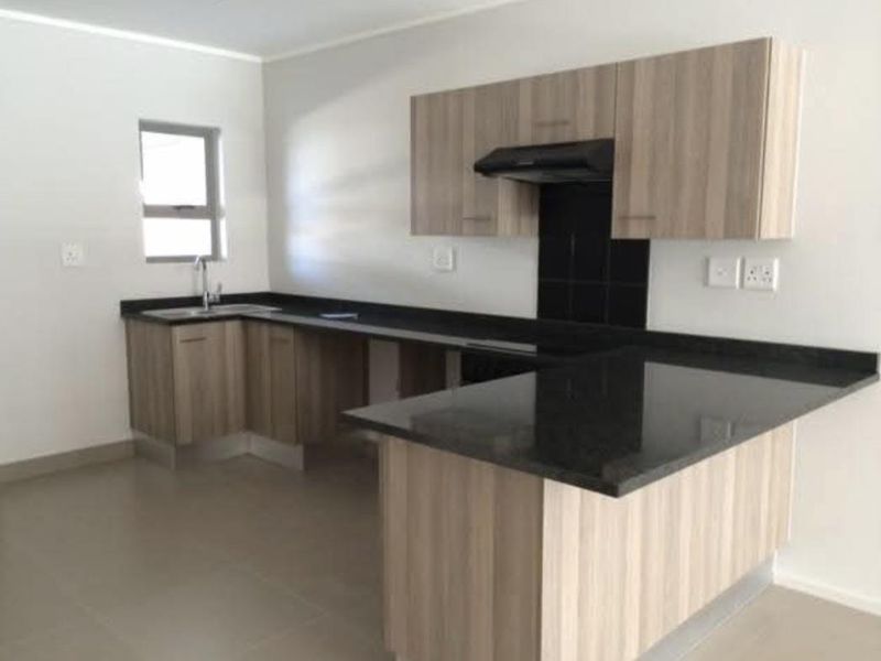Modern kitchen featuring light wood-grain cabinetry, dark granite countertops, a built-in extractor fan, and neutral tiled flooring in an open-plan layout.
