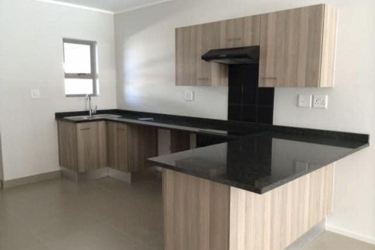 Modern kitchen featuring light wood-grain cabinetry, dark granite countertops, a built-in extractor fan, and neutral tiled flooring in an open-plan layout.