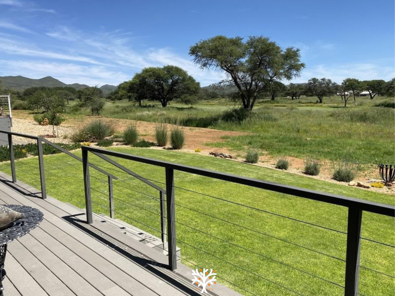 A modern elevated timber deck featuring a sleek metal and wire balustrade, offering expansive views over the landscaped garden and surrounding natural landscape.