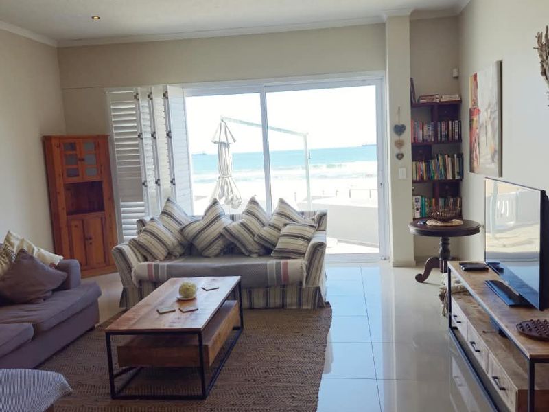 Bright living room featuring large sliding glass doors with ocean views, polished tile flooring, and built-in shelving.