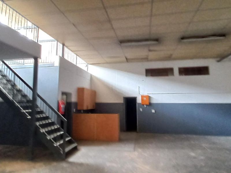 Spacious industrial utility area featuring a mezzanine level, metal staircase, suspended ceiling, and built-in cabinetry, suitable for storage or workshop use.