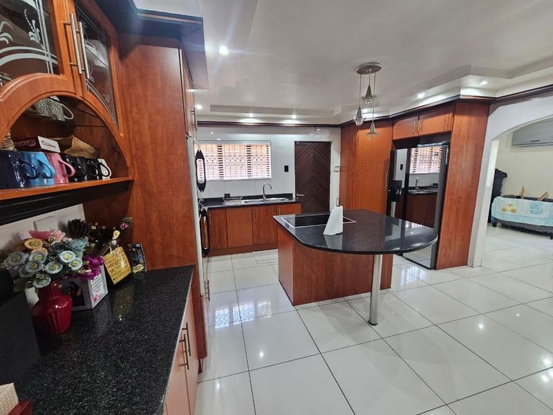 Spacious kitchen featuring dark granite countertops, extensive wooden cabinetry, a central island, and polished tiled flooring with recessed lighting.