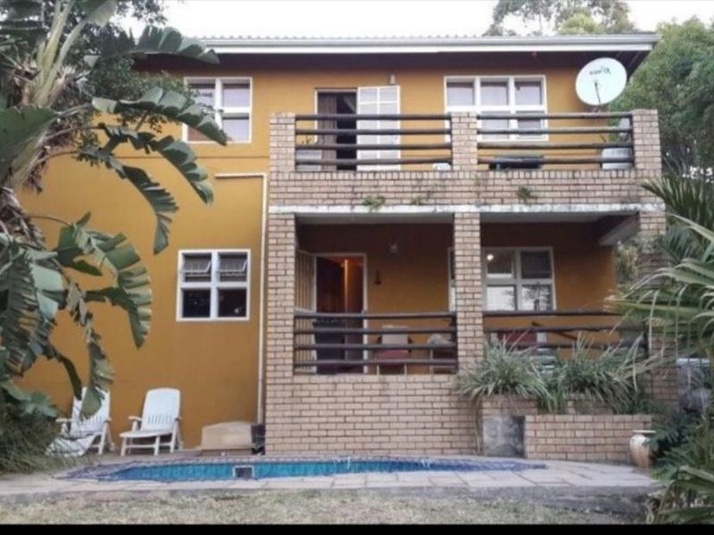 Rear view of a two-story house featuring a swimming pool, ground-level patio, and an upper-level balcony with brick detailing.