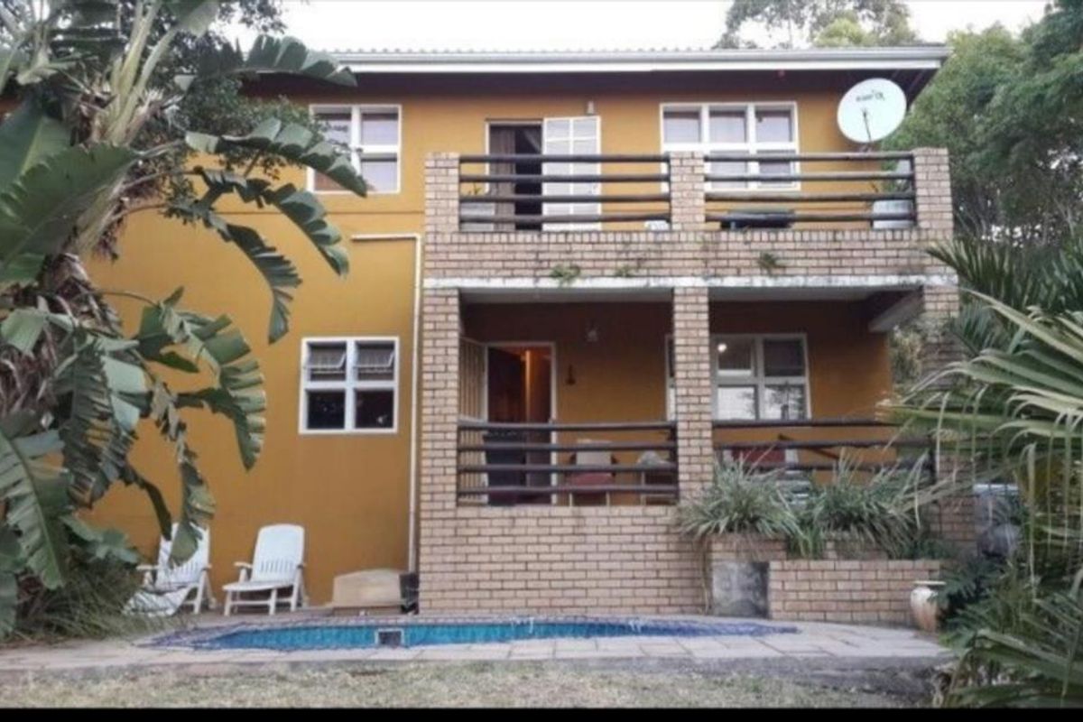 Rear view of a two-story house featuring a swimming pool, ground-level patio, and an upper-level balcony with brick detailing.
