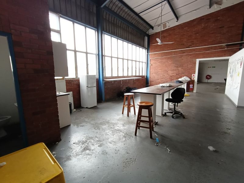 Spacious industrial utility area featuring exposed brick walls, high ceilings with steel trusses, large windows, and durable concrete flooring.
