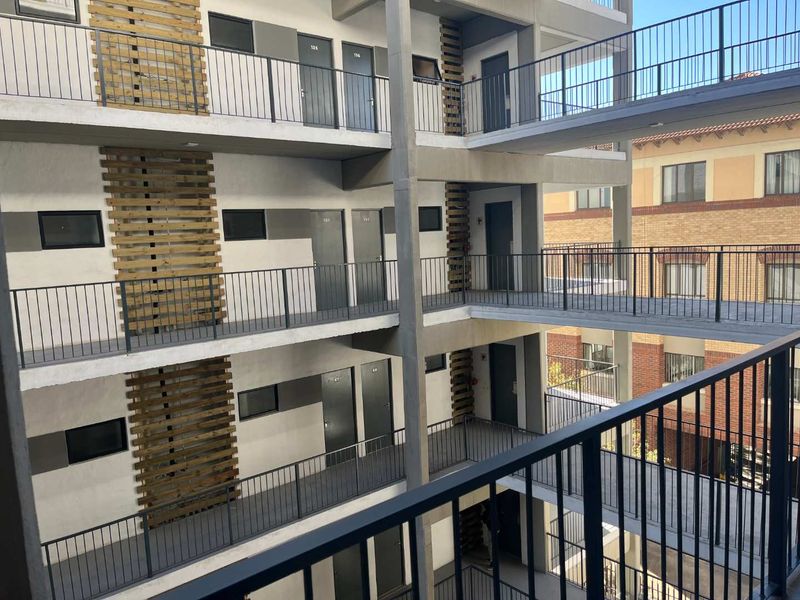 Exterior view of a modern apartment complex featuring multi-level concrete walkways, metal safety railings, and decorative timber slat wall accents.