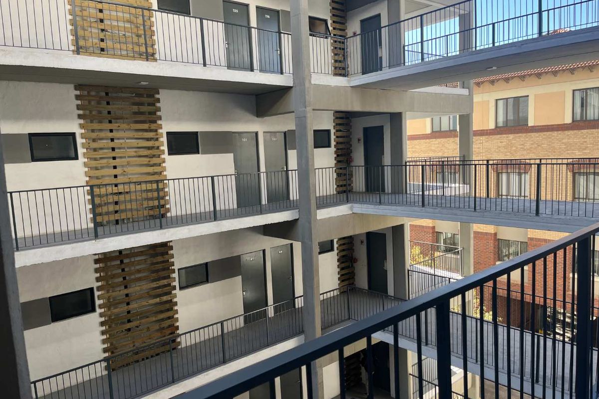 Exterior view of a modern apartment complex featuring multi-level concrete walkways, metal safety railings, and decorative timber slat wall accents.