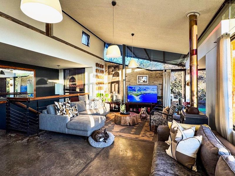Spacious living room featuring polished concrete floors, a stone feature wall, a freestanding fireplace, and high ceilings with large windows for natural light.
