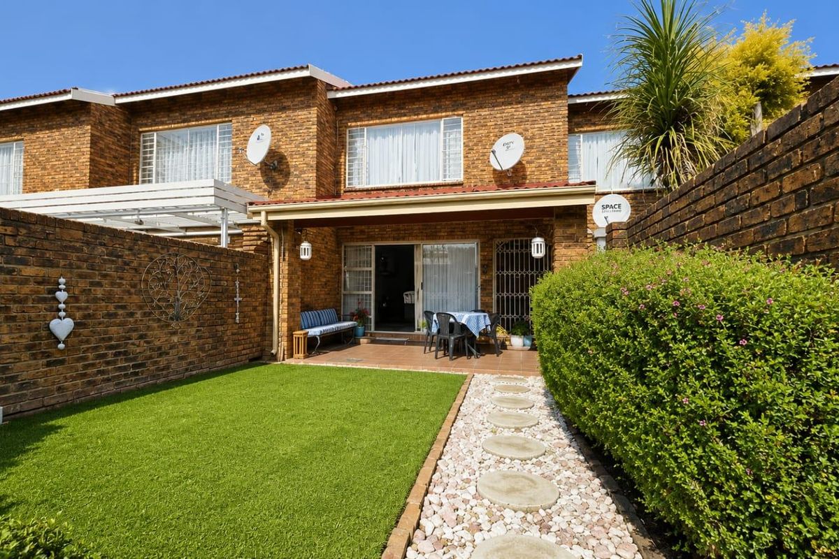 Rear view of a townhouse featuring a private garden with artificial lawn, stone pathway, and a covered patio area with sliding door access.