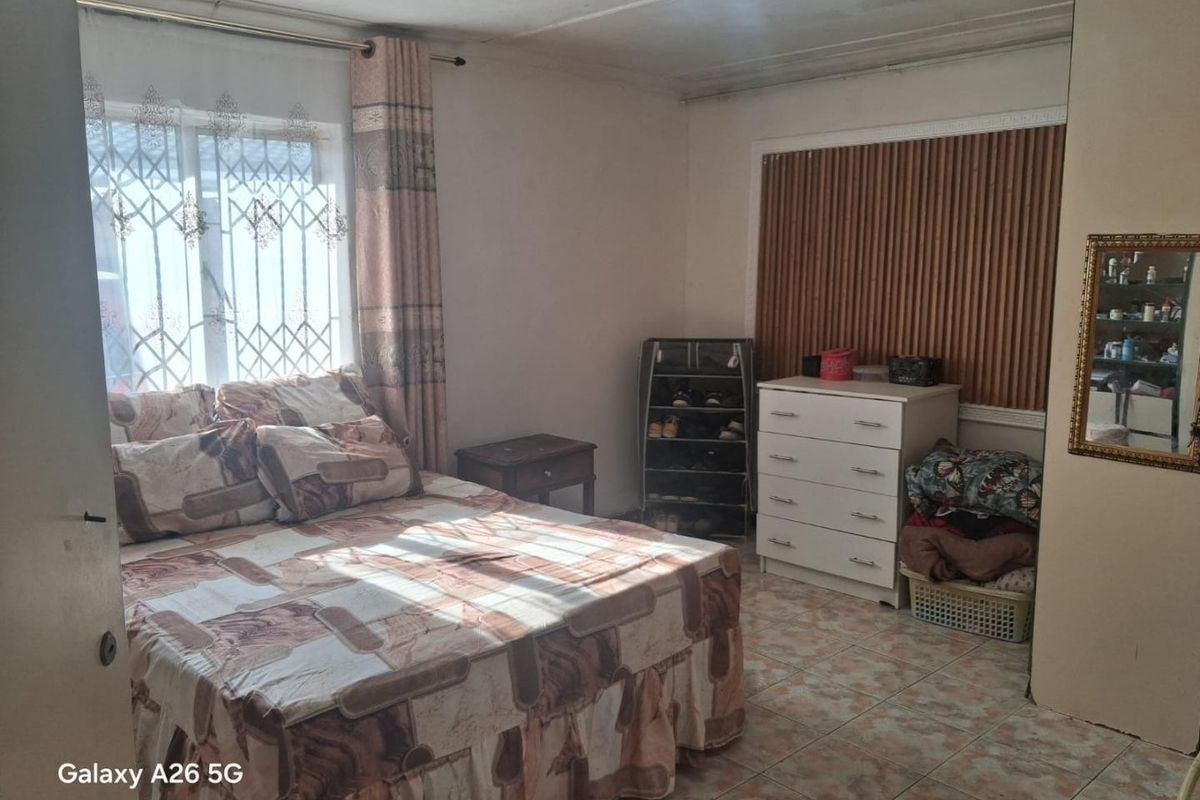 A bedroom featuring tiled flooring, security bars on the window, and window blinds. The ceiling shows visible signs of water damage and cracking.