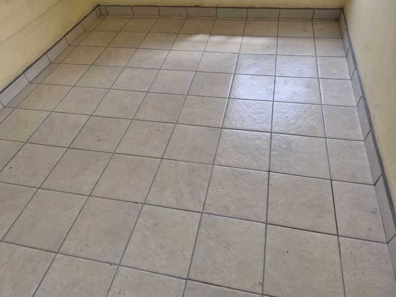 An empty room featuring neutral ceramic floor tiles and matching tiled skirting, providing a blank canvas for renovation or interior design updates.