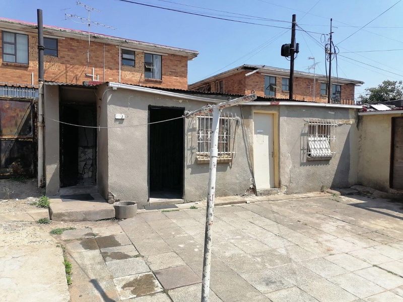 Rear exterior view of the property featuring a paved courtyard area with security bars on windows and weathered exterior wall finishes.
