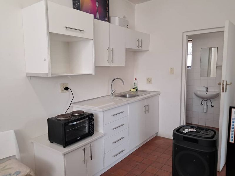 A compact kitchen featuring white cabinetry, a stainless steel sink, and tiled flooring, with an adjacent view into a small bathroom area.