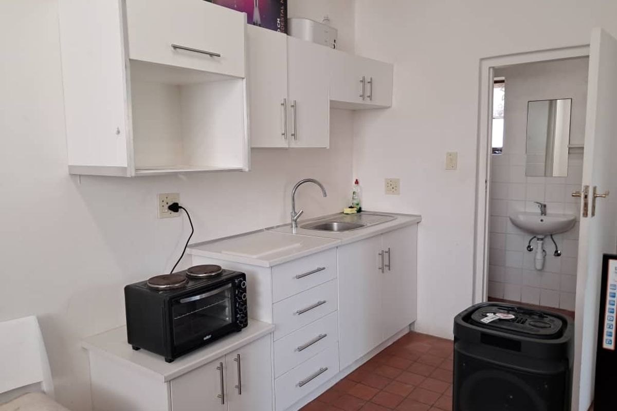 A compact kitchen featuring white cabinetry, a stainless steel sink, and tiled flooring, with an adjacent view into a small bathroom area.