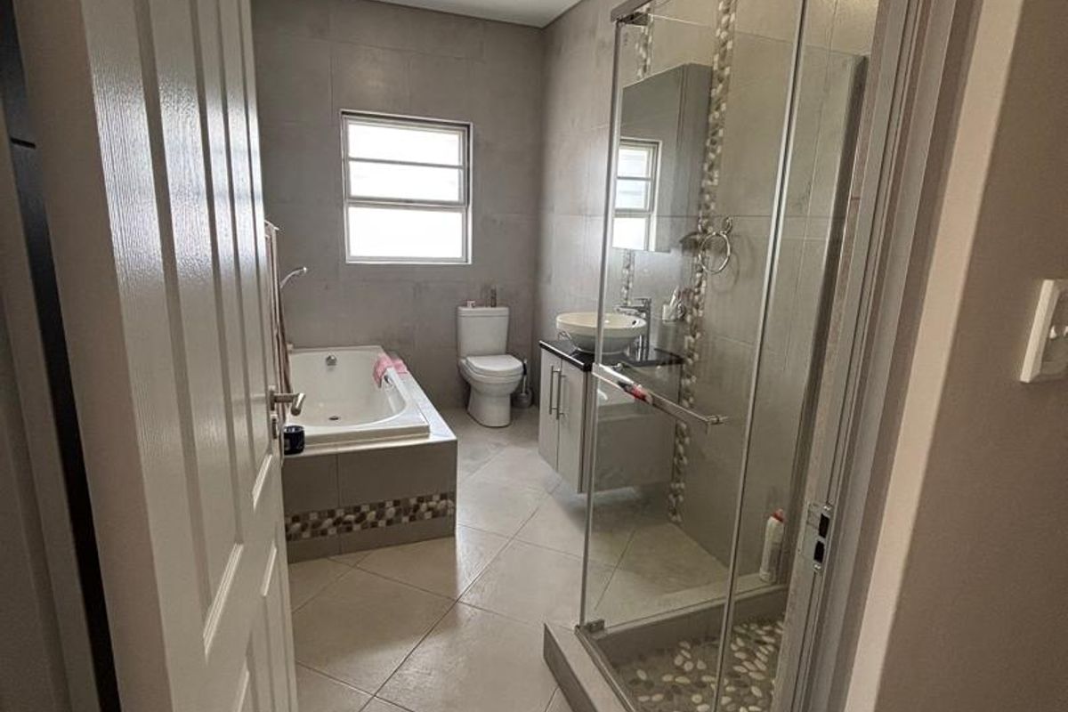 A well-appointed bathroom featuring a glass-enclosed shower with pebble flooring, a built-in bathtub, a vanity with a vessel sink, and neutral floor tiles.