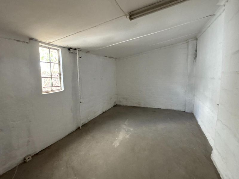 A basic, empty utility space featuring exposed concrete flooring, painted masonry walls, and a security-barred window, suitable for storage or workshop use.