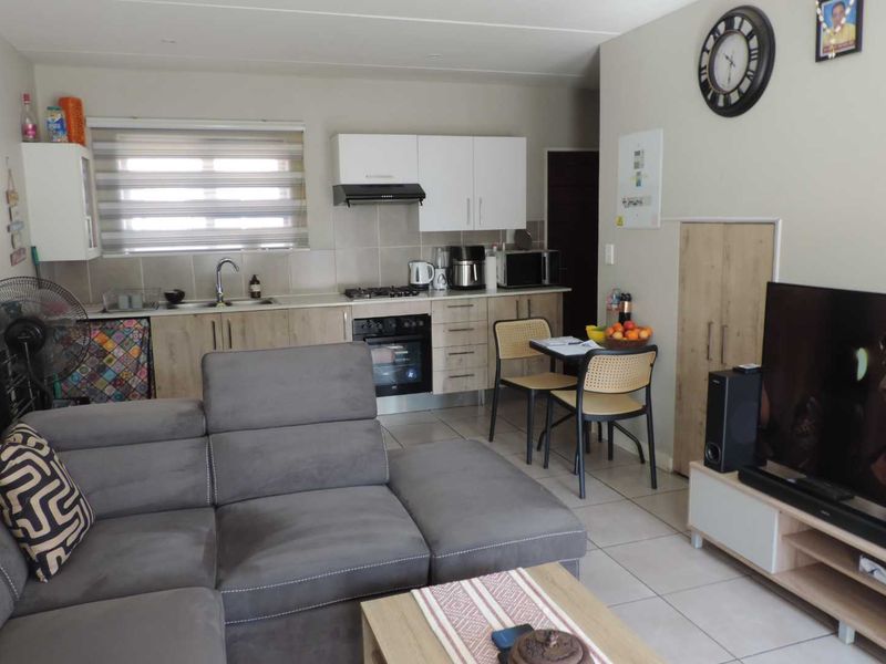 Open-plan living area featuring a compact kitchen with built-in cabinetry, gas hob, and tiled flooring, seamlessly integrated with the lounge space.