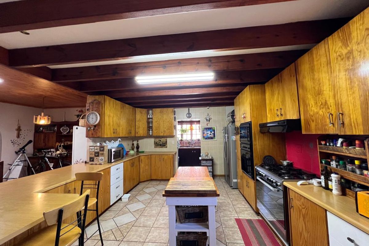 Spacious kitchen featuring extensive wooden cabinetry, exposed timber ceiling beams, a central island, and a built-in oven and gas hob setup.