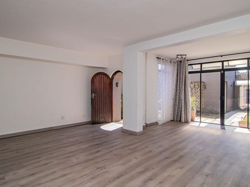 A bright, open-plan living area featuring modern laminate flooring, a structural column, and large sliding glass doors providing access to the rear patio.