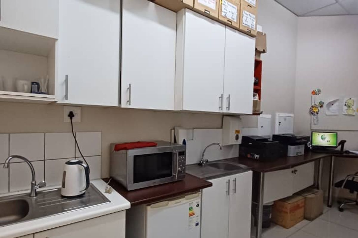 A functional office kitchenette featuring built-in cabinetry, a stainless steel sink, tiled splashback, and integrated workspace area.