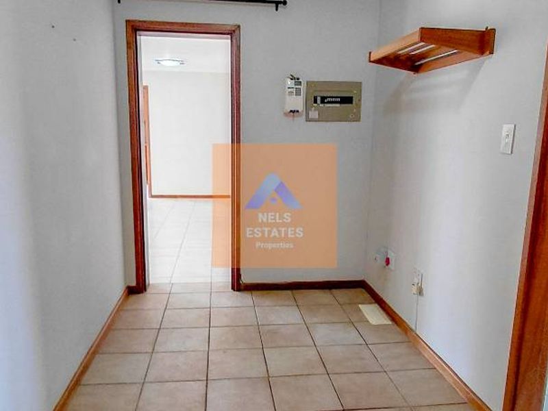 A clean, tiled hallway featuring a ceiling light, wall-mounted shelving, and an accessible electrical distribution board, leading into an adjacent room.
