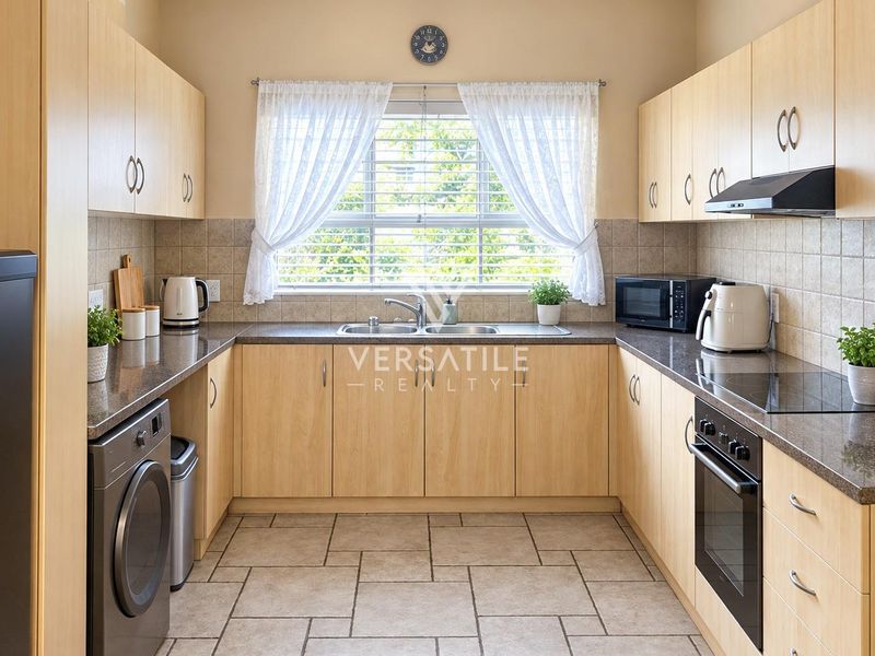 A functional U-shaped kitchen featuring light wood cabinetry, granite countertops, tiled backsplash, and integrated appliances including an oven and hob.