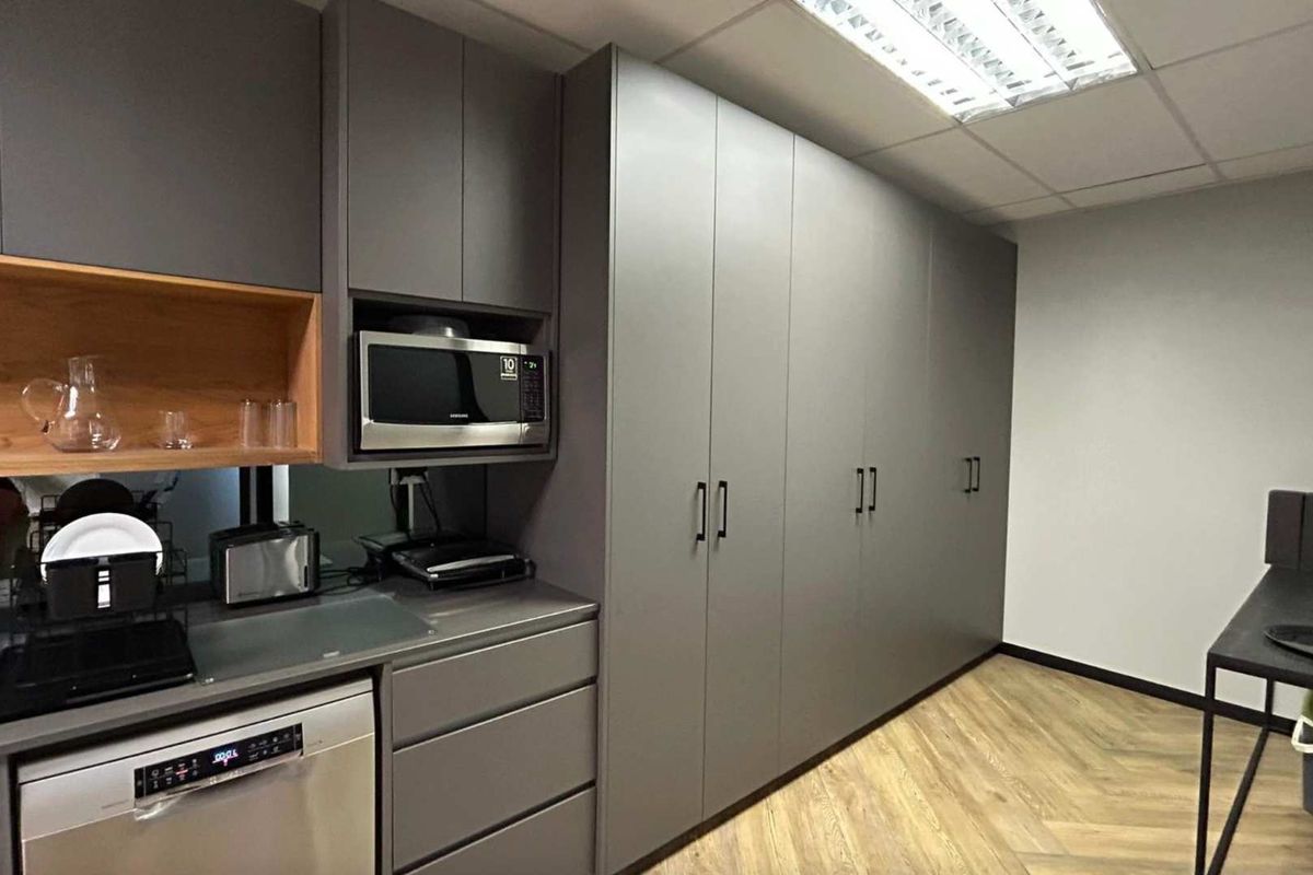 Modern office kitchenette featuring sleek grey cabinetry, integrated appliances, wood-look flooring, and professional recessed lighting.