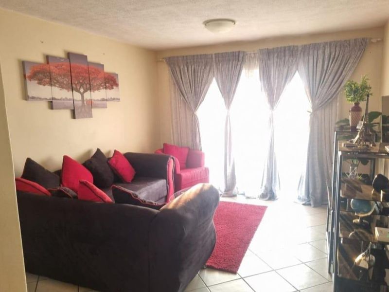 A living room featuring tiled flooring and large windows with curtain tracks, providing natural light to the space.