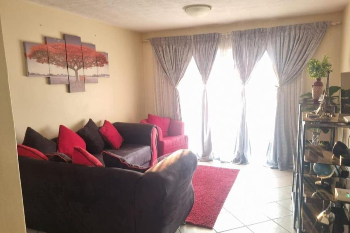 A living room featuring tiled flooring and large windows with curtain tracks, providing natural light to the space.